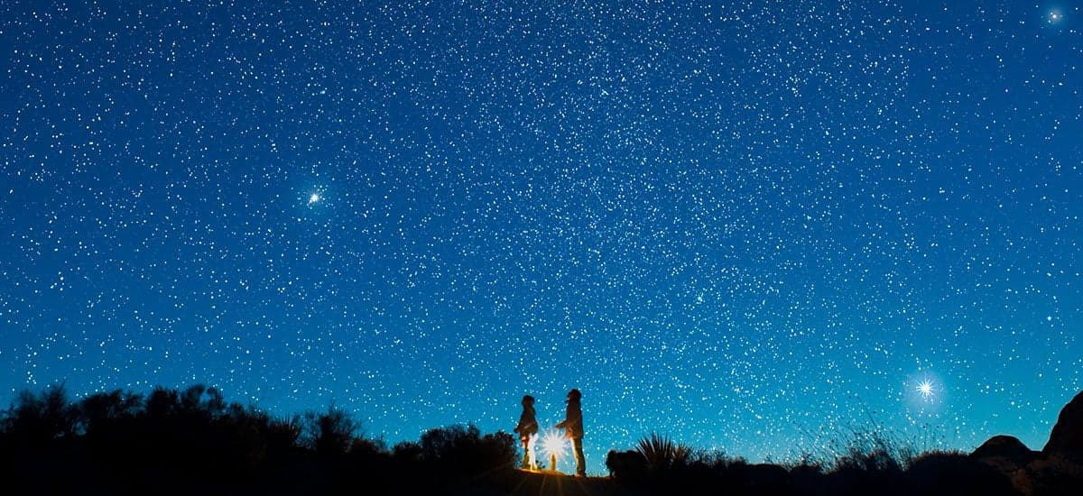 A star-filled night sky over a desert horizon.